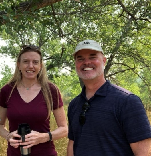 Jennifer Shanahan and Todd Bridges stand smiling with trees in the background.