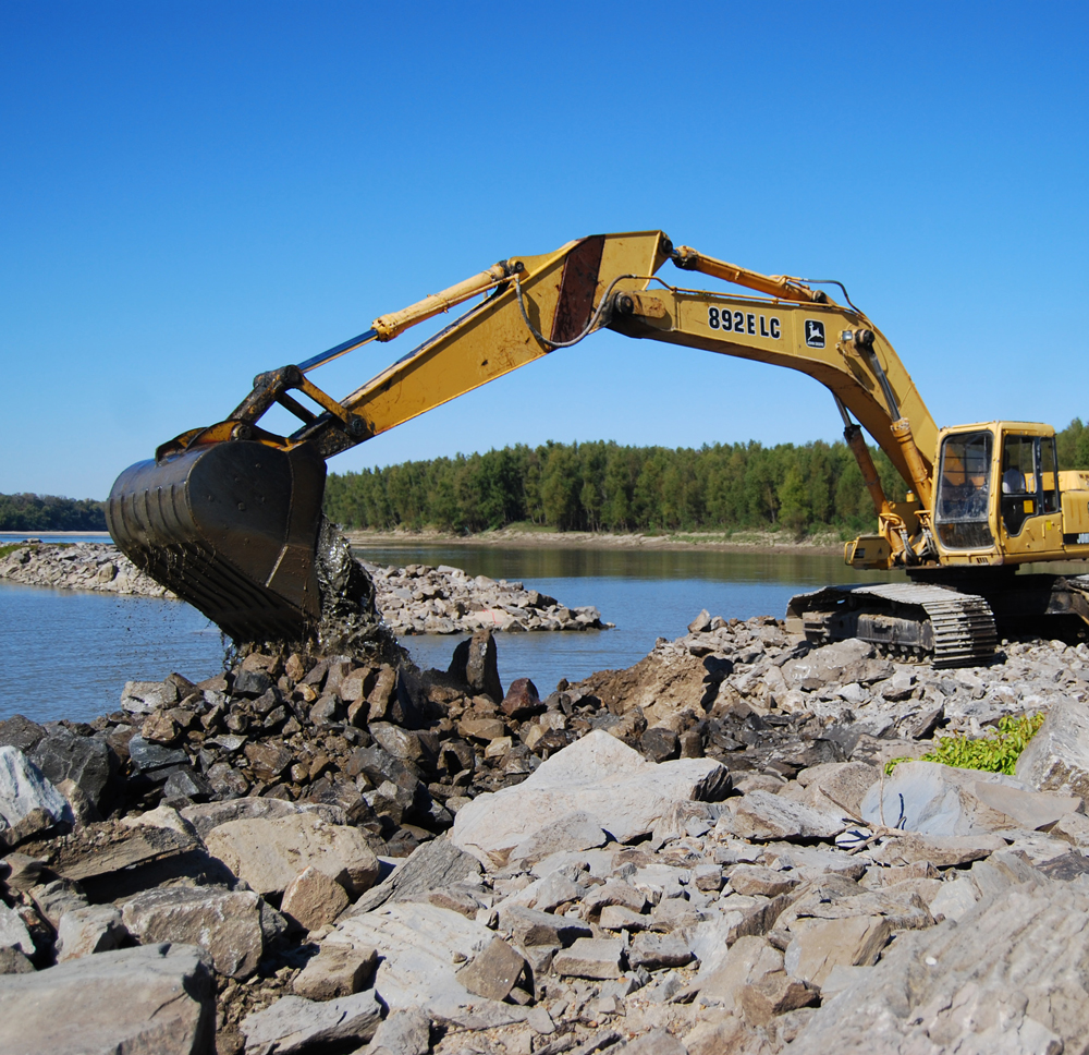 A trackhoe excavates rock to make a notch in a dike as part of the project. (Photo by USACE Memphis District)