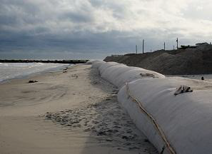 Long barrier away from shore wrapped in canvas. To the left is the sandy beach and water.